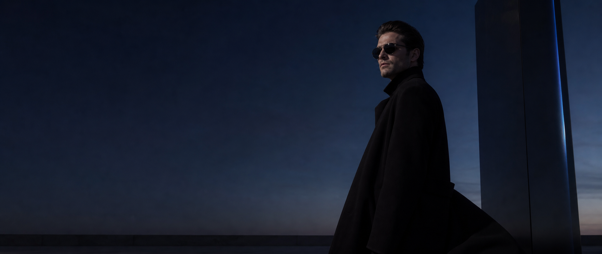 Man in a dark overcoat wearing sunglasses beside a blue-lit rooftop monolith